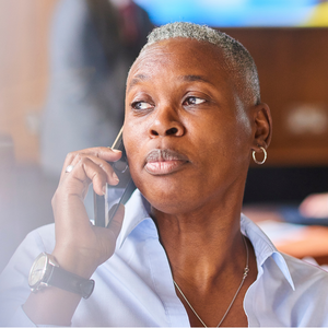 A Black woman with short gray hair holds a phone receiver to her ear in an office setting