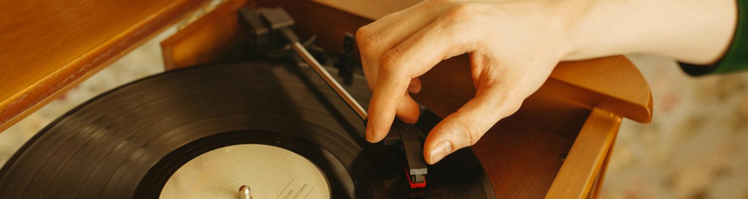 A person's hand steadies a phonograph needle before placing it on a record 