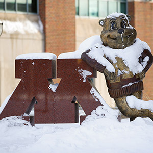 U of M mascot Goldy Gopher leans again a giant maroon marble M with snow blanketing its shoulders