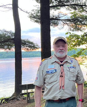 Eric Neff in his Eagle Scout uniform stands in front of a lake at sunset