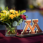 Vase with greenery and maroon and gold flowers alongside a block M award on a table