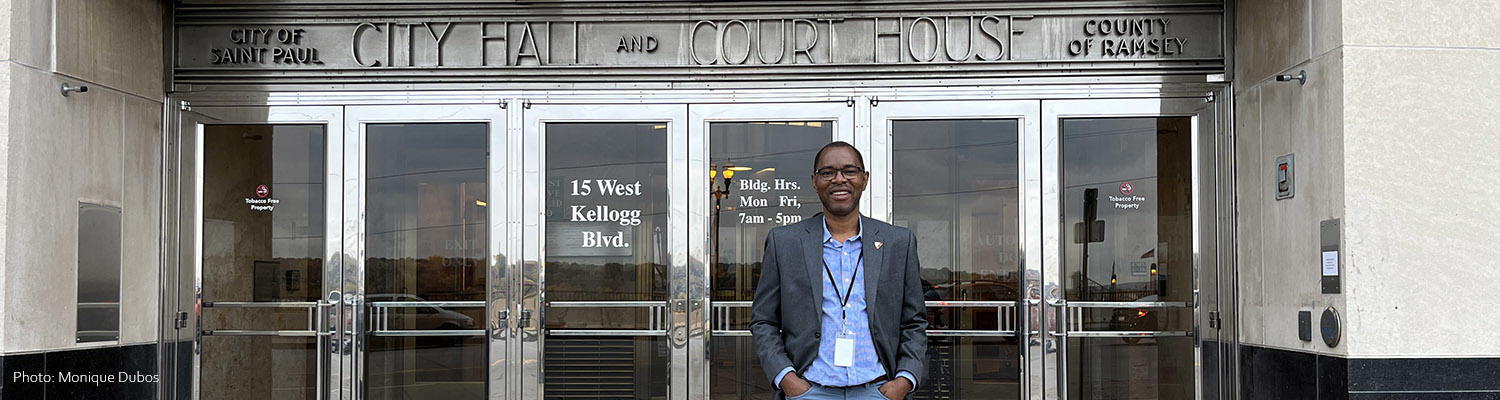 Jules Atangana stands in front of the silver metal Art Deco doors of St. Paul City Hall