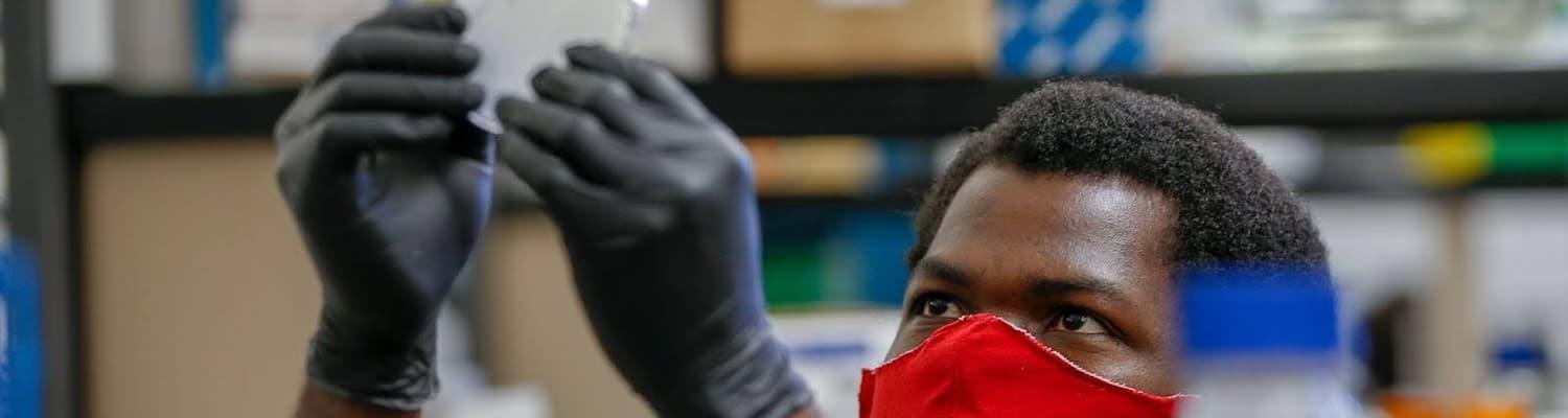 Student wearing a mask and black gloves holds up a petri dish